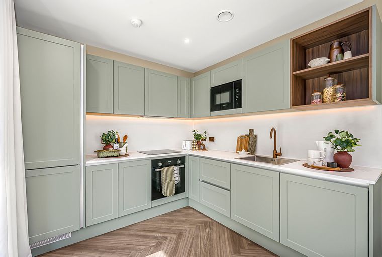 A modern kitchen with sage-green cabinets, a built-in microwave, and a sink.