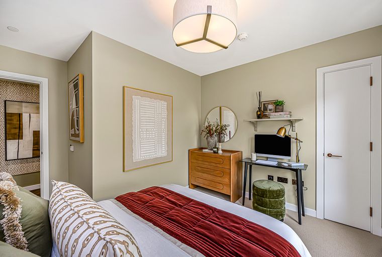 A bedroom with a bed, dresser, desk, and artwork.