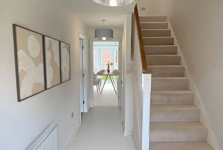 A hallway with a carpeted staircase, artwork on the wall, and a view into a dining room.