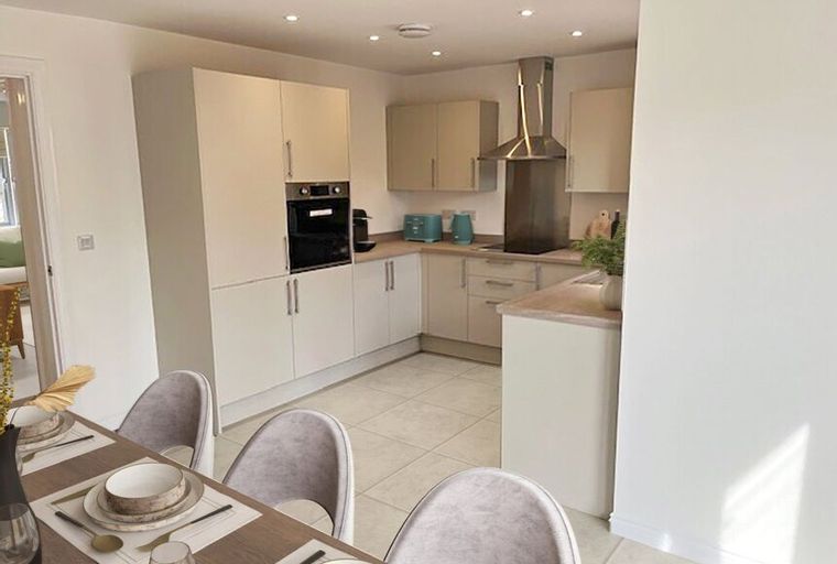 A modern kitchen with cream cabinets, integrated appliances, and a stainless steel extractor hood.