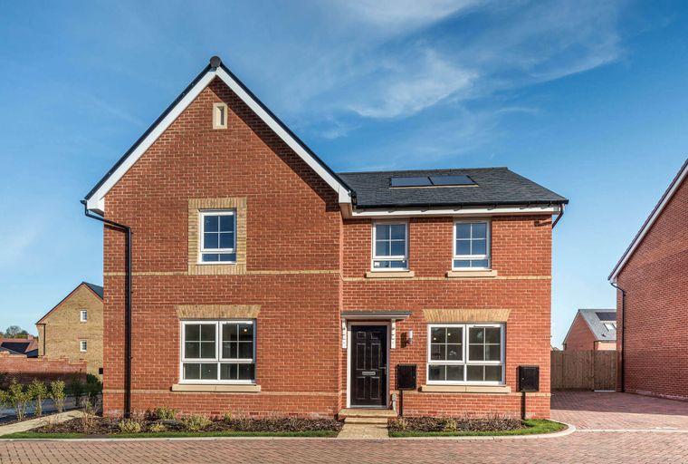 A red brick house with white-framed windows and a dark front door under a blue sky.