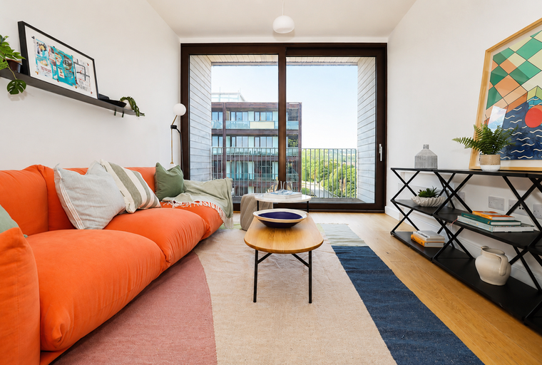 A living room with an orange sofa, coffee table, and a large window overlooking a building.
