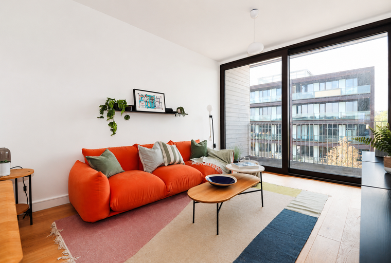 A living room with an orange sofa, coffee table, and a large window overlooking a building.