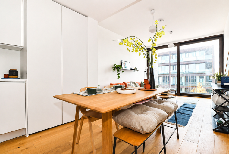 A dining table set for a meal with chairs and cushions in a room with large windows.