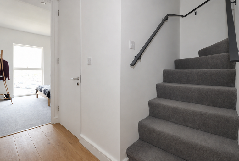 A hallway with a carpeted staircase and a doorway leading to a bedroom.