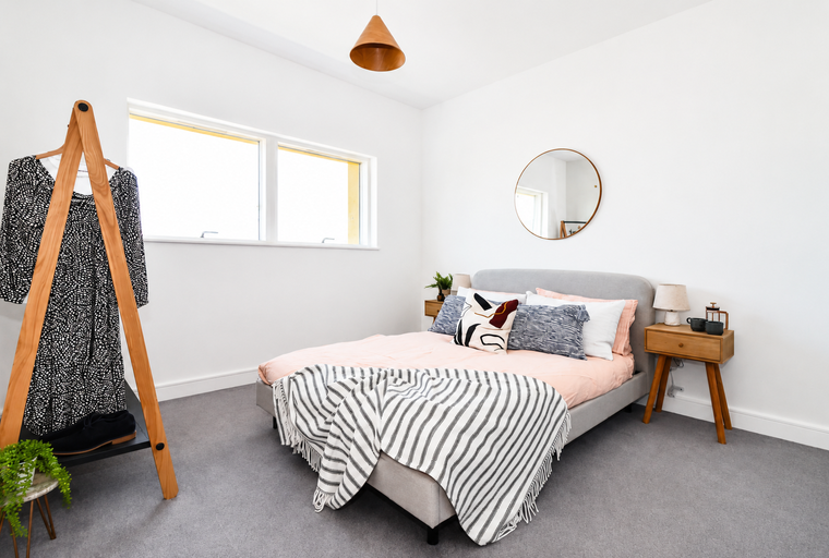 A bedroom with a bed, clothing rack, and a mirror.