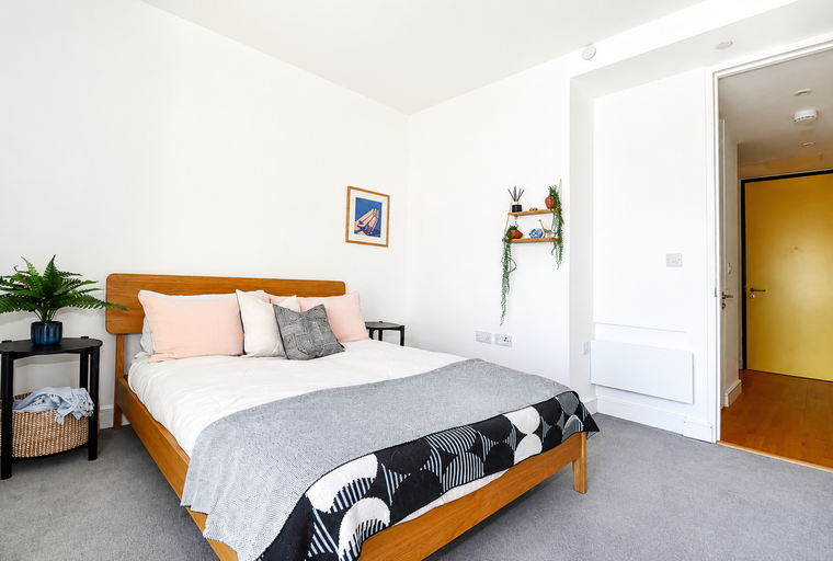 A bedroom with a bed, pillows, a throw blanket, and a side table.