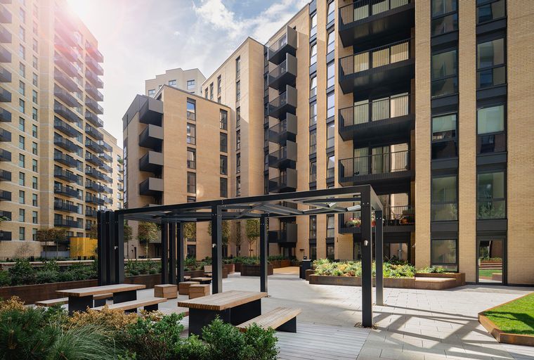 A courtyard with picnic tables and benches in front of modern apartment buildings.
