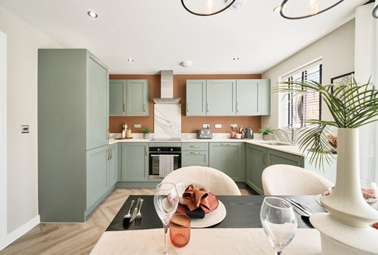 A modern kitchen and dining area with sage green cabinets, a terracotta backsplash, and a dining table set for a meal.