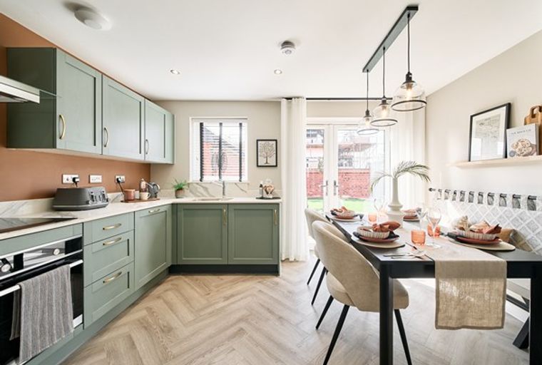A kitchen and dining area with sage green cabinets, a black dining table, and herringbone flooring.