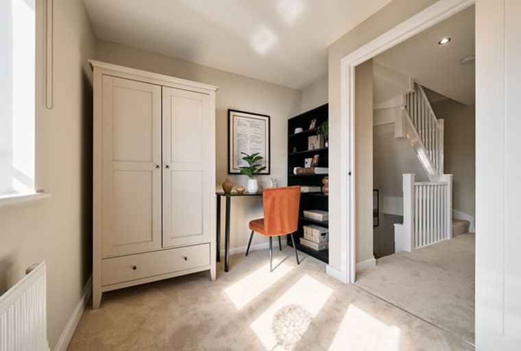 A home office with a wardrobe, desk, chair, and bookshelf, with a staircase visible through a doorway.