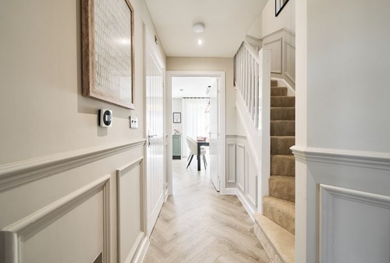 A hallway with a staircase, wainscoting, and a herringbone floor.