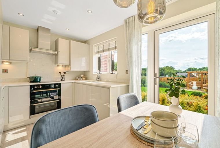 A kitchen and dining area with a table set for a meal, overlooking a garden through glass doors.