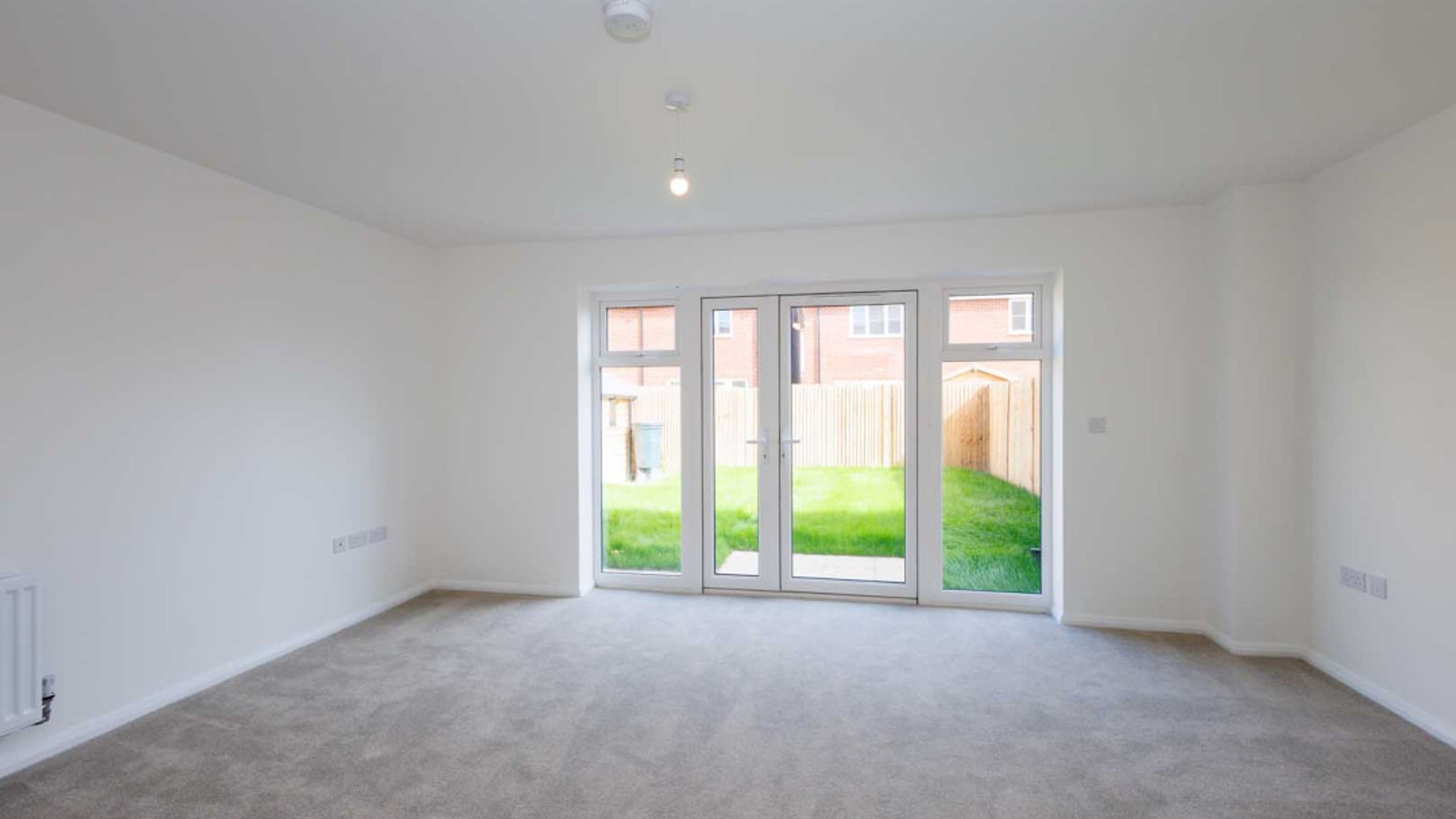 A living room with grey carpet, white walls, and double doors leading to a garden.