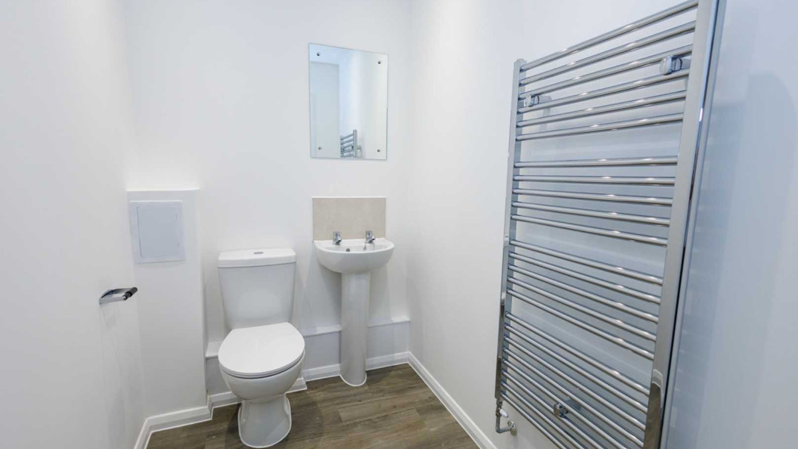 A bathroom with a toilet, a sink, a mirror, and a towel warmer.