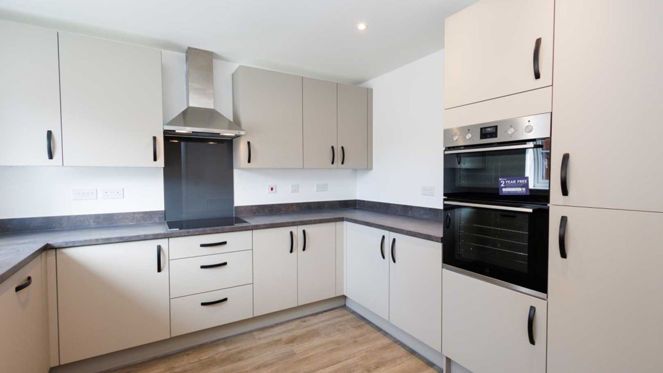 A modern kitchen with cream cabinets, a stainless steel range hood, and a double oven.