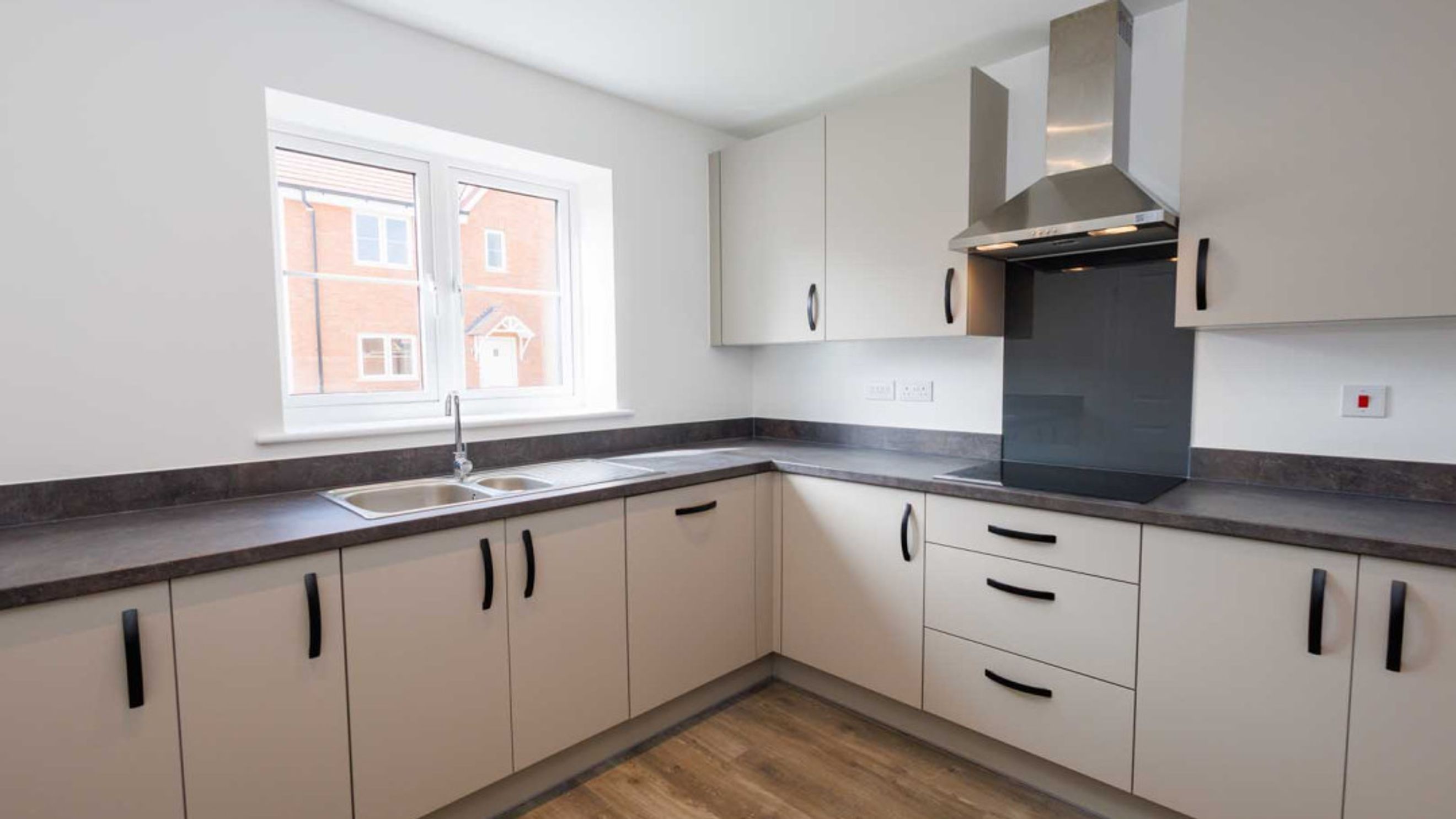 A modern kitchen with cream cabinets, a double sink, and a window.