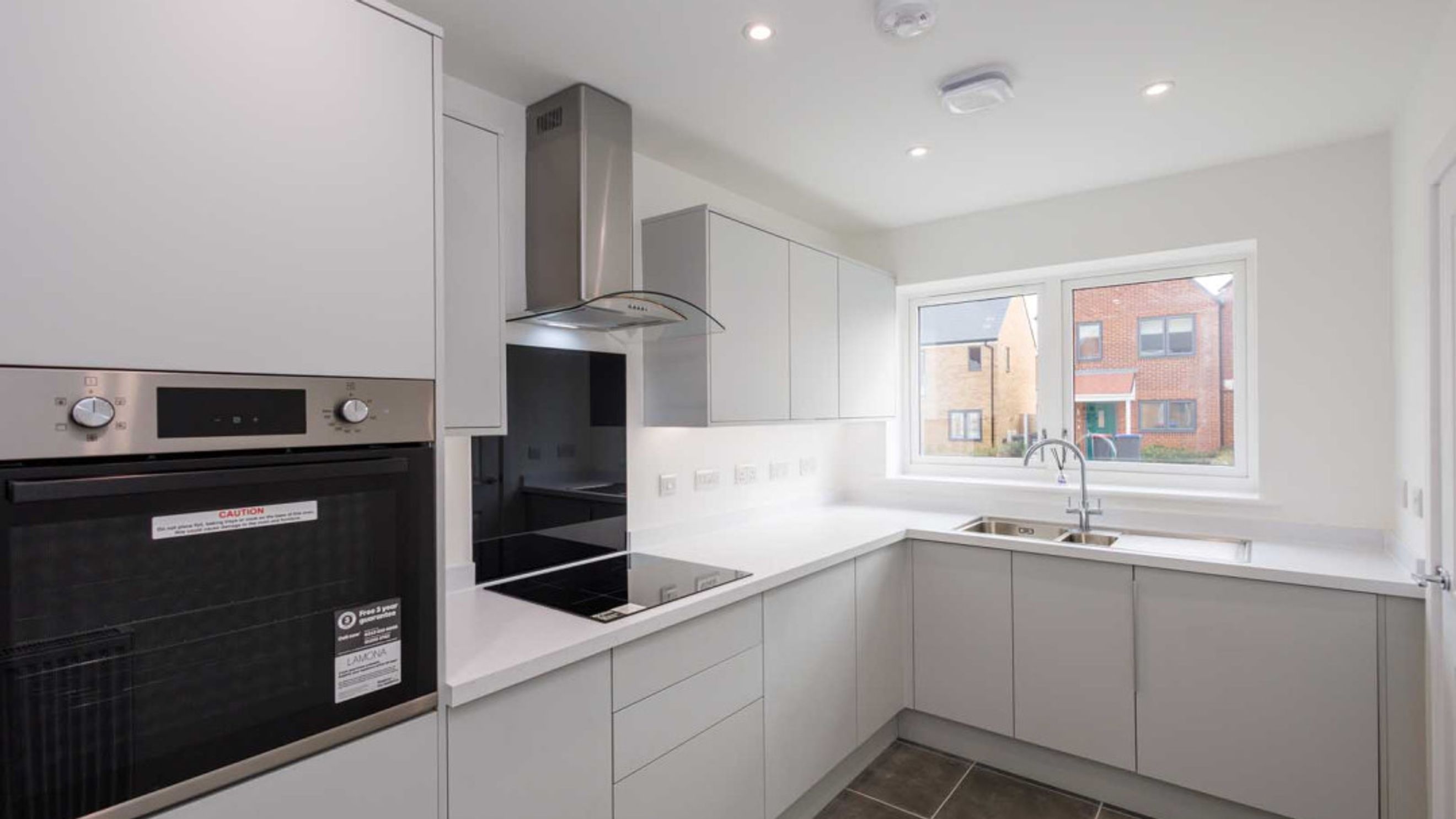 A modern kitchen with grey cabinets, a white countertop, a built-in oven, and a window.