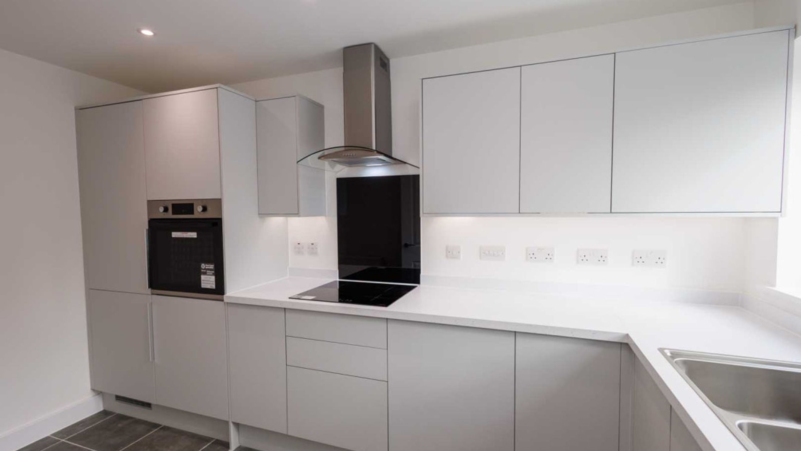 A modern kitchen with light grey cabinets, a built-in oven, an induction hob, and a stainless steel extractor hood.