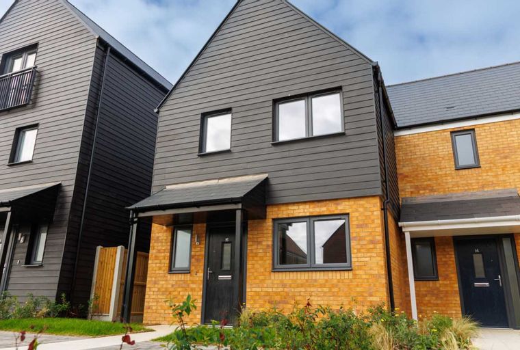 A row of modern townhouses with dark grey cladding and yellow brick exteriors.