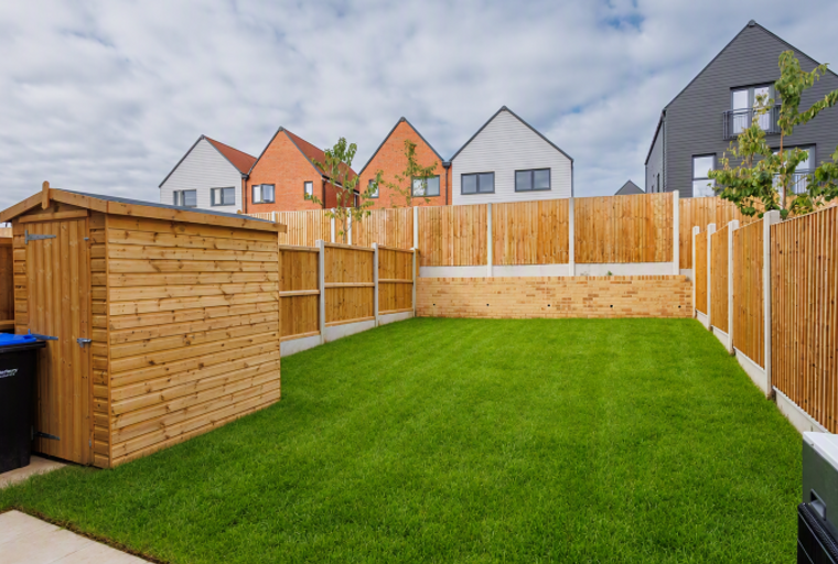 A backyard with a wooden shed, green lawn, and a wooden fence.