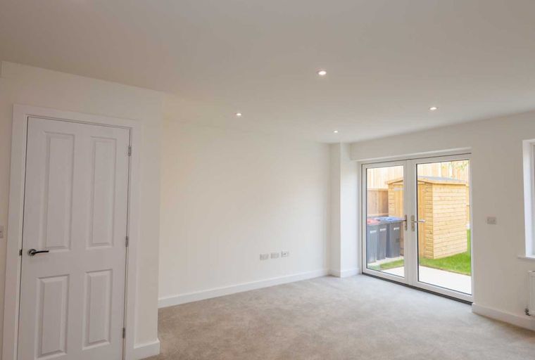 A room with a white door, grey carpet, and double glass doors leading outside.