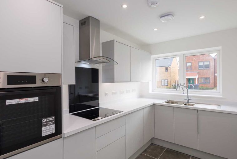 A modern kitchen with grey cabinets, a white countertop, a built-in oven, and a window.