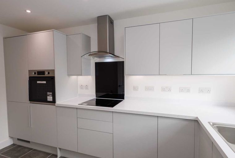 A modern kitchen with light grey cabinets, a built-in oven, an induction hob, and a stainless steel extractor hood.