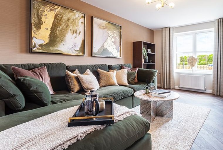 A living room with a large green sectional sofa, throw pillows, artwork, and a coffee table.