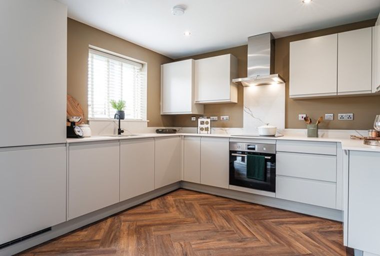 A modern kitchen with light-colored cabinets, a herringbone wood floor, and a stainless steel range hood.