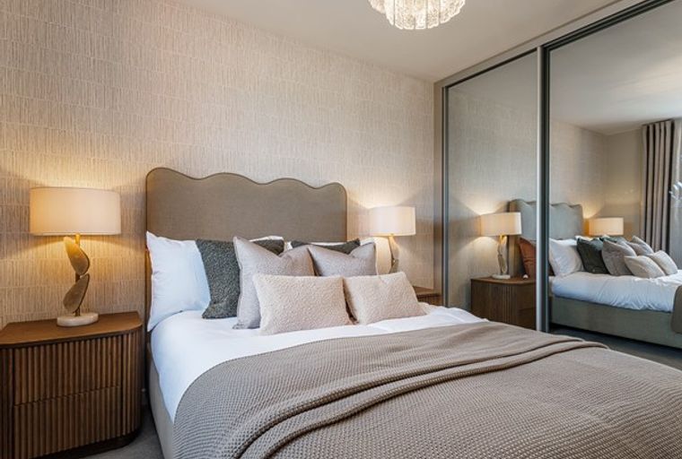 A bedroom with a bed, bedside tables, lamps, and a mirrored wardrobe.