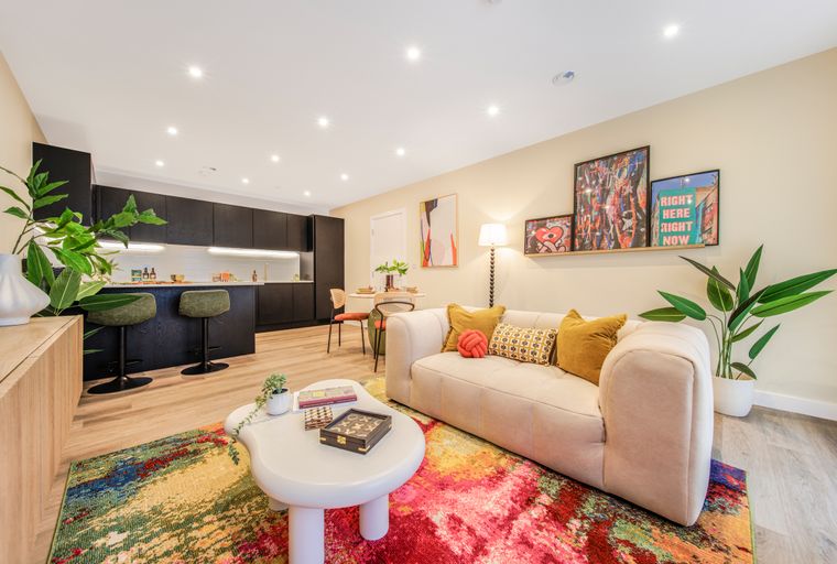 A living room and kitchen area with a sofa, coffee table, bar stools, and artwork.