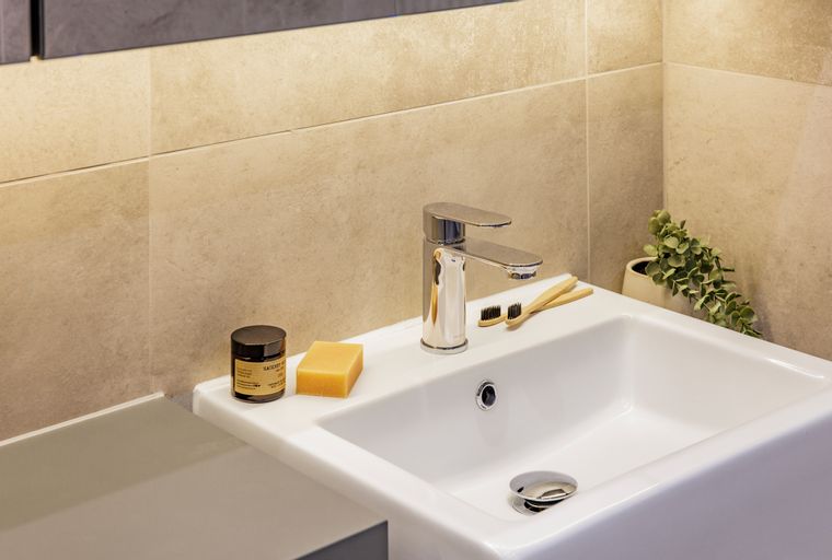 A bathroom sink with a faucet, soap, toothbrushes, and a plant.