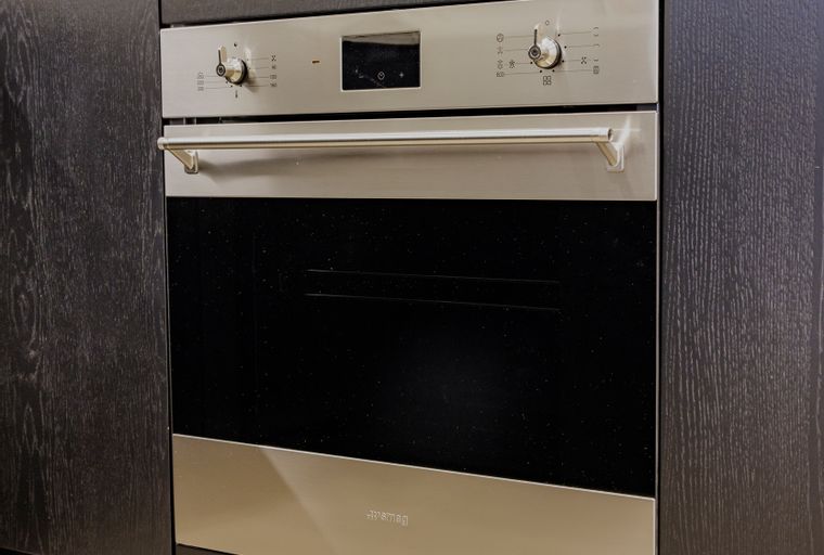 A built-in oven with a stainless steel handle and digital display, set within dark wood cabinetry.