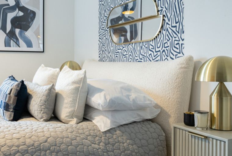 A bedroom with a bed, pillows, a bedside lamp, and artwork.