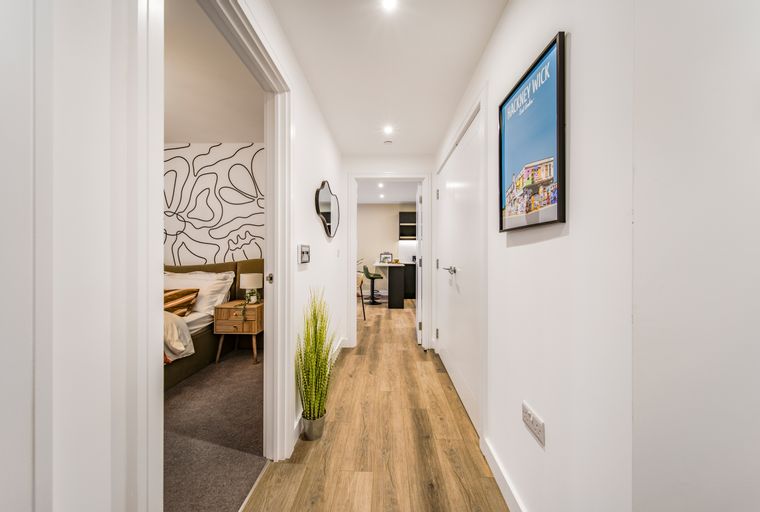 A hallway with wooden floors, a framed picture, and doorways leading to a bedroom and a kitchen.