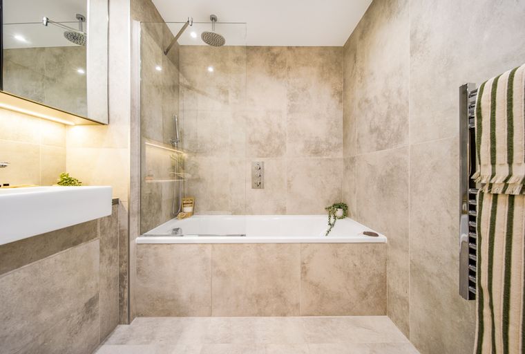 A bathroom with a bathtub, shower, sink, and tiled walls.
