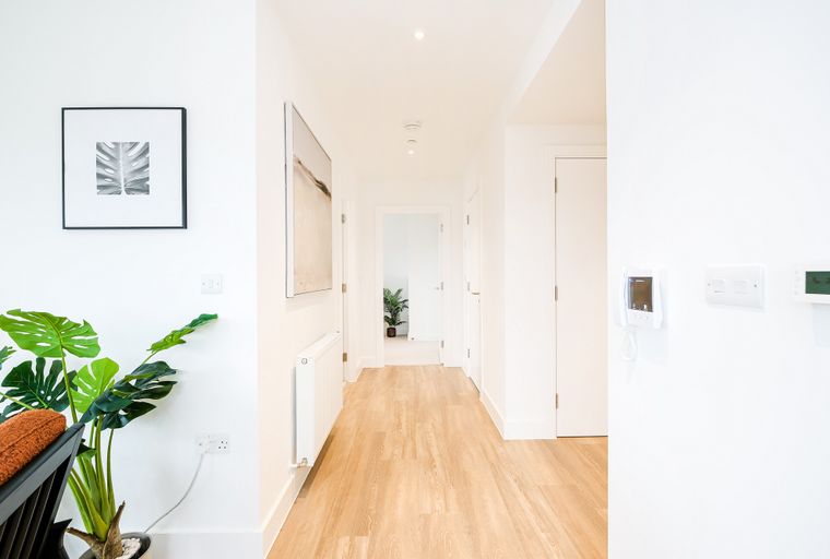 A hallway with wooden floors, doors, and artwork on the wall.