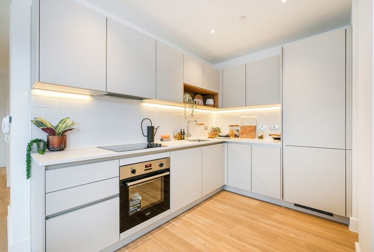A modern kitchen with light gray cabinets, a white subway tile backsplash, and light wood flooring.