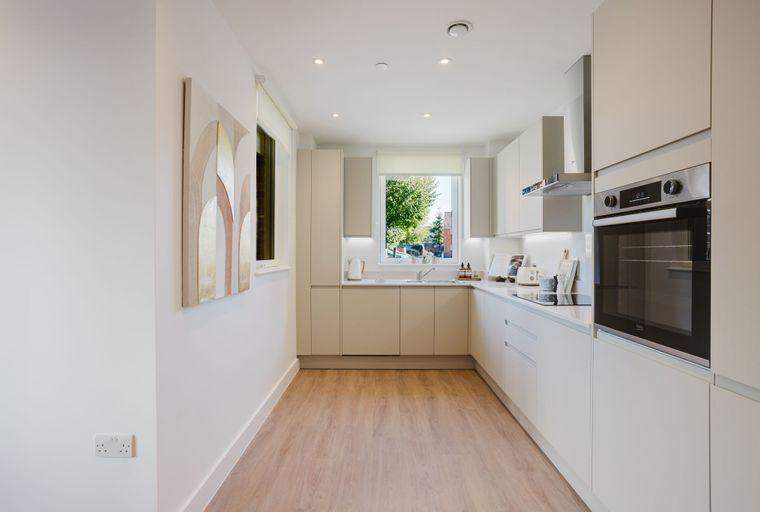 A modern kitchen with light-colored cabinets, a built-in oven, and a window overlooking trees.