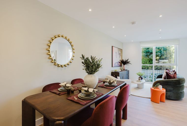 A dining area with a wooden table and chairs, a mirror on the wall, and a living area with a green armchair and an orange table.