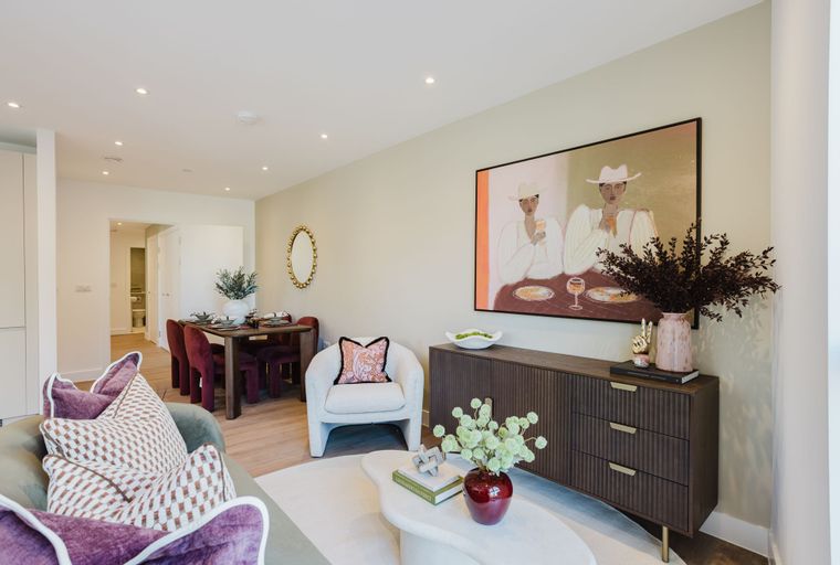 A living and dining room with a sofa, armchair, dining table, and artwork.