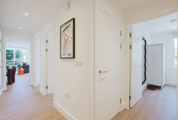 A hallway with multiple doors, light wood flooring, and a framed picture on the wall.