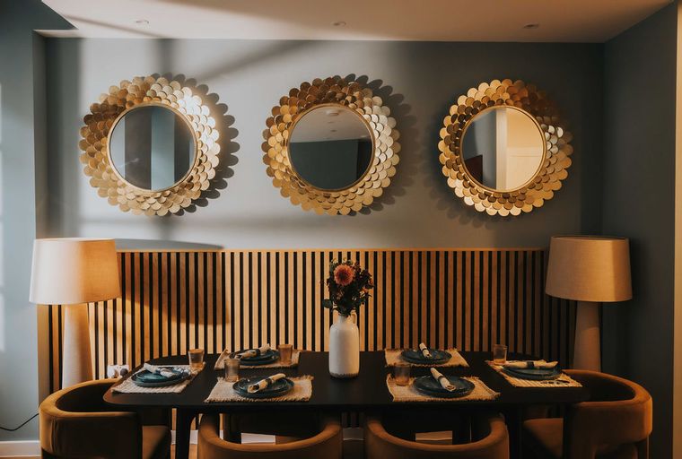 A dining room table set for four with three gold mirrors on the wall.
