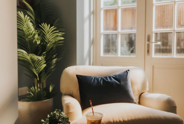 A chair with a pillow, a table with drinks and plants in front of French doors.