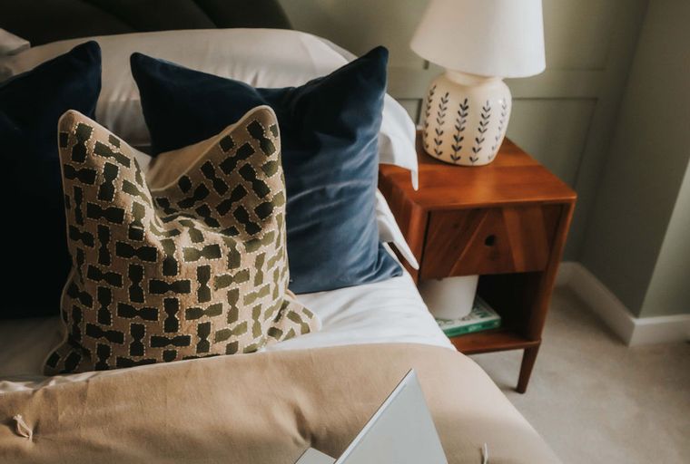 A bedroom with a bed, pillows, a laptop, and a bedside table.