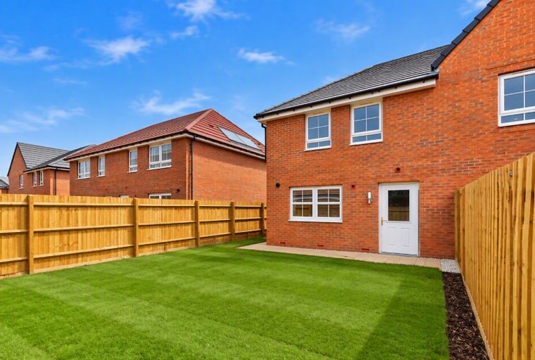 A backyard with a manicured lawn and a wooden fence in front of a brick house.