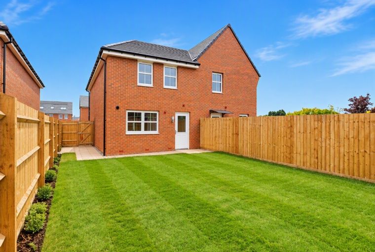 A backyard with a mown lawn and a wooden fence in front of a brick house.
