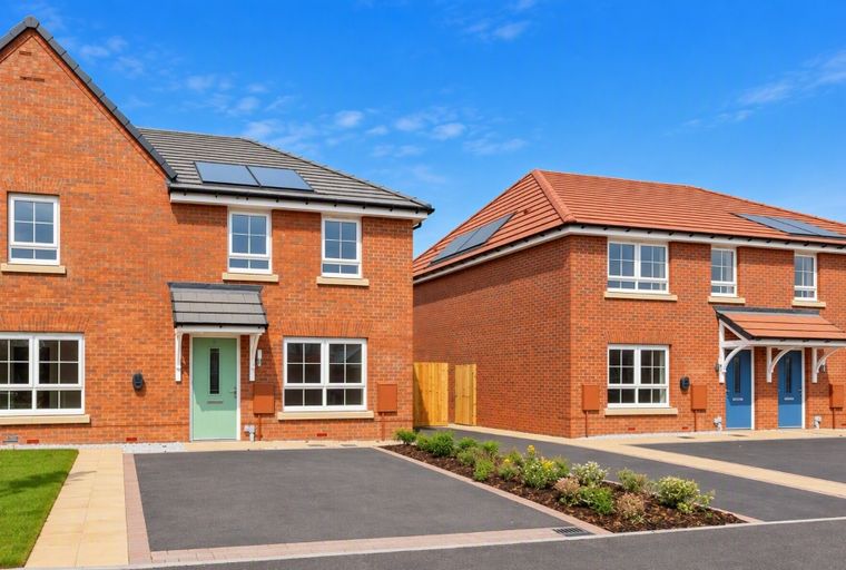 A row of modern brick houses with solar panels on the roofs and paved driveways under a clear blue sky.