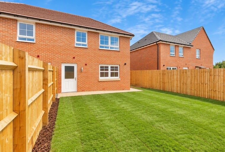 A backyard of a brick house with a wooden fence and a green lawn under a blue sky.